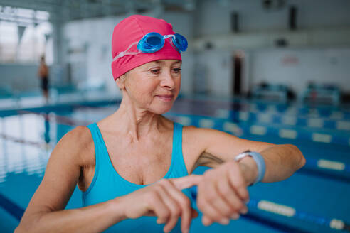 Eine ältere Frau stellt ihre Smartwatch vor dem Schwimmen im Hallenbad ein. - HPIF04936