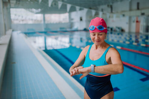 Eine ältere Frau stellt ihre Smartwatch vor dem Schwimmen im Hallenbad ein. - HPIF04938