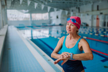 Eine ältere Frau stellt ihre Smartwatch vor dem Schwimmen im Hallenbad ein. - HPIF04939