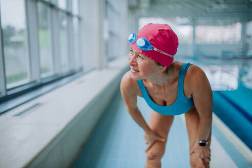Eine aktive ältere Frau, die sich auf das Schwimmen im Hallenbad vorbereitet. - HPIF04941