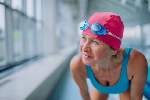 Eine Nahaufnahme einer aktiven älteren Frau, die sich auf das Schwimmen im Hallenbad vorbereitet. - HPIF04942
