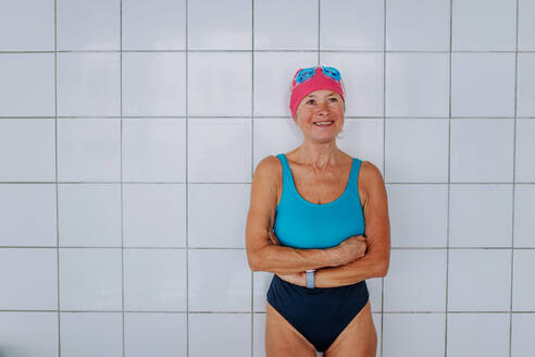 Ein aktiver Senior Schwimmer Frau steht gegen weiße Fliesen Wand drinnen im Schwimmbad. - HPIF04945