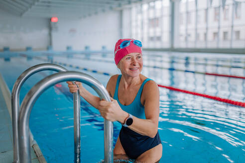 Eine aktive ältere Schwimmerin benutzt eine Leiter, um ins Schwimmbad zu gelangen. - HPIF04947