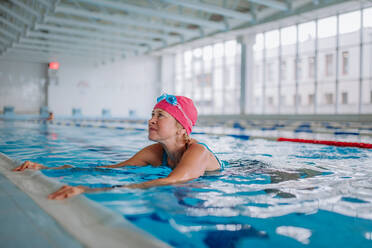 Eine glückliche ältere Frau im Schwimmbad, die sich am Rand festhält. - HPIF04949