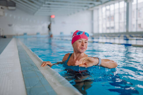 Eine ältere Frau schaut beim Schwimmen im Hallenbad auf ihre Smartwatch. - HPIF04950