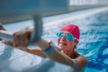 Eine aktive ältere Schwimmerin hält sich am Startblock fest und bereitet sich auf das Schwimmen im Hallenbad vor. - HPIF04954