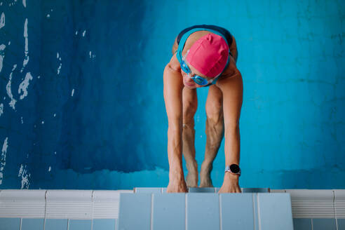 Draufsicht auf eine aktive ältere Schwimmerin, die sich am Startblock im Hallenbad festhält. - HPIF04955
