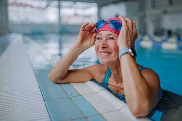 Eine glückliche ältere Frau im Schwimmbad, die sich an den Rand lehnt. - HPIF04958