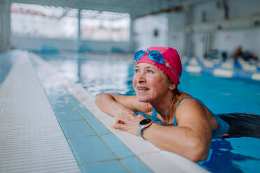 Eine glückliche ältere Frau im Schwimmbad, die sich an den Rand lehnt. - HPIF04959