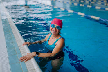 Eine glückliche ältere Frau im Schwimmbad, die sich an den Rand lehnt und in die Kamera schaut. - HPIF04960