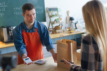 Ein fröhlicher junger Kellner mit Down-Syndrom, der Kunden in einem Restaurant zum Mitnehmen bedient, Konzept der sozialen Integration. - HPIF04981