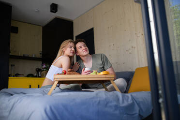 Ein junges, hübsches, verliebtes Paar sitzt im Bett und frühstückt gemeinsam. - HPIF04997