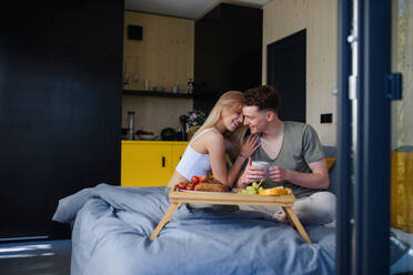Ein junges, hübsches, verliebtes Paar sitzt im Bett und frühstückt gemeinsam. - HPIF04998