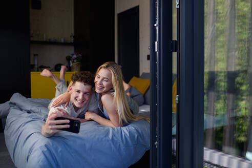 Ein junges, glückliches, verliebtes Paar liegt morgens in ihrem neuen Zuhause in einem kleinen Haus im Bett und macht ein Selfie, ein nachhaltiges Wohnkonzept. - HPIF05002