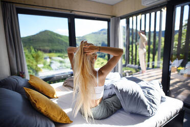 Eine Rückansicht einer jungen Frau im Bett am Morgen mit ihrem Mann auf der Terrasse in ihrem neuen Haus in einem kleinen Haus, einem nachhaltigen Wohnkonzept. - HPIF05007