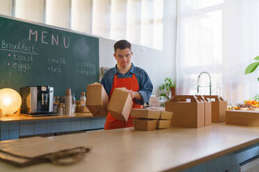 A cheerful young Down Syndrome waiter working in take away restaurant, social inclusion concept. - HPIF05072