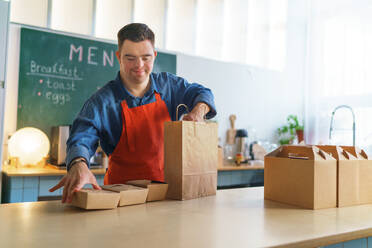 A cheerful young Down Syndrome waiter working in take away restaurant, social inclusion concept. - HPIF05078