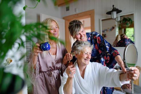 Happy senior women friends in bathrobes having fun indoors in a bathroom, selfcare concept. - HPIF05117