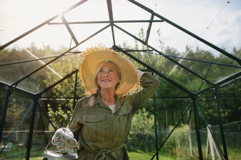 A happy senior gardener woman holding watering can in greenhouse at garden. - HPIF05122