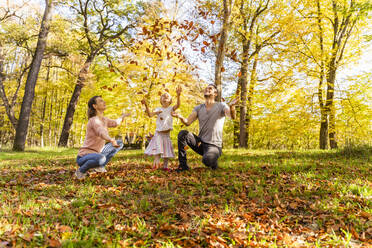 Verspielte Eltern mit Tochter, die Herbstblätter in den Park wirft - DIGF19673