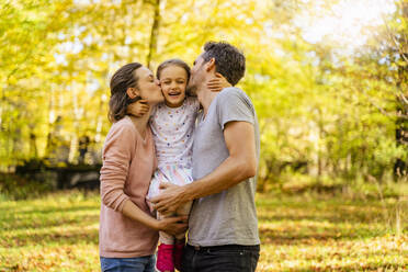 Parents with eyes closed kissing daughter in park - DIGF19682