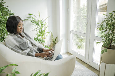 Young businesswoman using laptop sitting in armchair at home - OSF01236