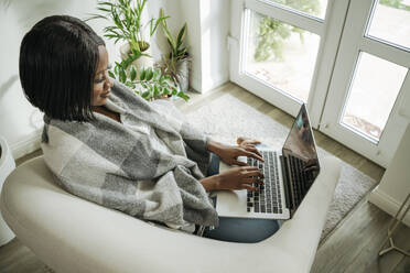 Lächelnde Geschäftsfrau mit Laptop im Sessel zu Hause - OSF01237