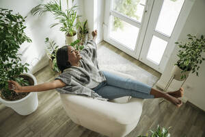 Glückliche Frau streckt die Arme aus und entspannt sich im Sessel zu Hause - OSF01238