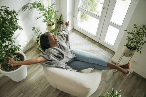 Happy woman stretching arms relaxing in armchair at home - OSF01238