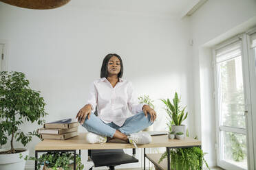 Businesswoman with eyes closed meditating on desk at home office - OSF01240