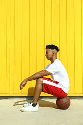 Man sitting on basketball in front of yellow wall - SYEF00049