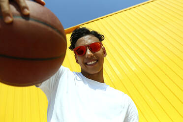 Smiling man with basketball in front of yellow wall - SYEF00054