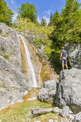 Deutschland, Bayern, Männlicher Tourist steht auf einem Felsbrocken vor dem Rappinbach-Wasserfall - FOF13247