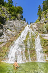 Deutschland, Bayern, Männlicher Wanderer beim Entspannen im Teich des Glasbachwasserfalls im Sommer - FOF13250