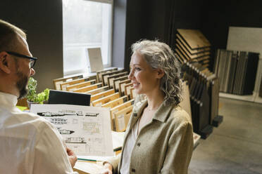 Smiling businesswoman looking at colleague holding construction plan in architect's office - SEAF01526