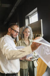 Two colleagues holding printout of a house in architect's office - SEAF01543