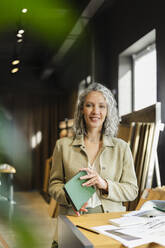 Porträt einer lächelnden Architektin, die ein Notizbuch im Büro hält - SEAF01571