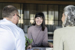 Lächelnde Frau bei einem Treffen mit einem Geschäftsmann und einer Geschäftsfrau im Büro - SEAF01591