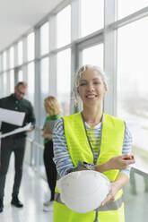 Smiling woman wearing protective workwear with colleagues in background in office - SEAF01652