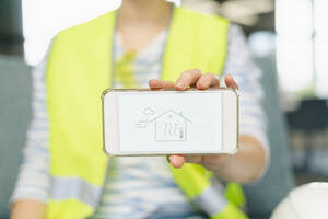 Woman wearing reflective clothing holding mobile phone with house on display - SEAF01666