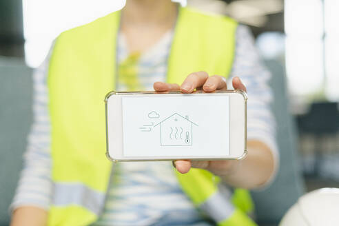 Frau in reflektierender Kleidung hält Mobiltelefon mit Haus auf dem Display - SEAF01666