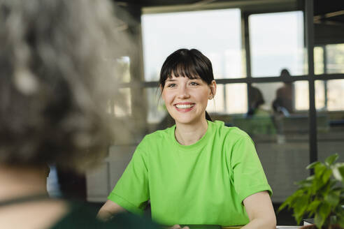 Lächelnde Frau mit Kollege in grünem T-Shirt im Büro - SEAF01712
