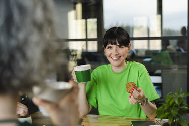 Glückliche Frau mit grünem T-Shirt in einer Pause im Büro - SEAF01719