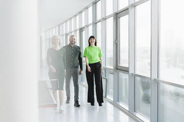 Three happy business people in green clothing walking on office floor - SEAF01729