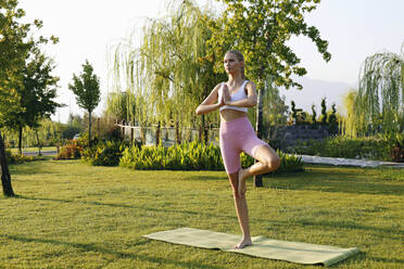 Junge Frau in Vrikshasana-Pose im Park - SYEF00092