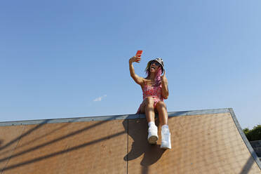 Glückliche Frau gestikuliert und nimmt Selfie durch Handy auf dem Dach des Hauses - SYEF00114