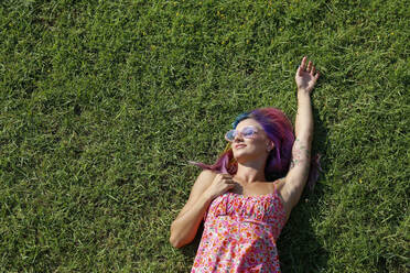 Smiling woman lying on grass enjoying sunny day - SYEF00115