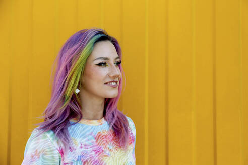 Lächelnde junge Frau mit buntem Haar vor einer gelben Wand - SYEF00117