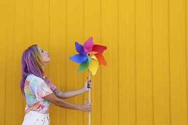 Woman blowing colorful pinwheel toy in front of yellow wall - SYEF00127