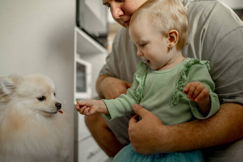 Vater mit süßer Tochter füttert Hund zu Hause - ANAF00709